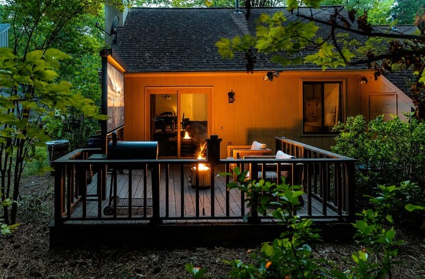 A wooden cabin with a deck, a fireplace, and a dining area.