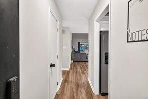 Un couloir au plancher de bois mène à une cuisine équipée d’un réfrigérateur.