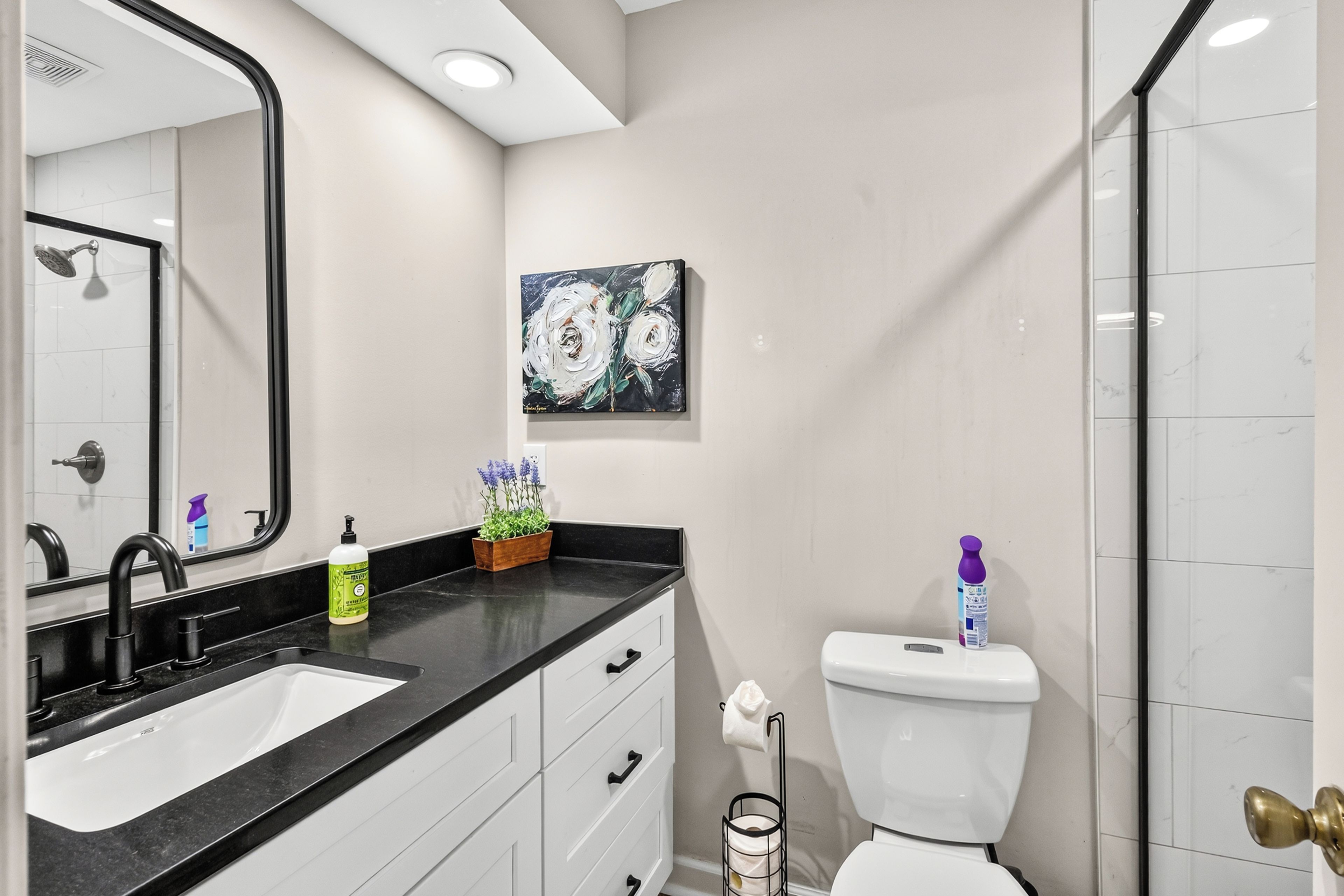 Een badkamer met een zwart aanrechtblad, een wit wastafelmeubel en een toilet met een papieren handdoekhouder.