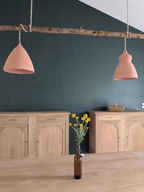 A kitchen with wooden cabinets, a hanging light fixture, and a vase with yellow flowers on a wooden table. - L'Atelier - Maison avec piscine face au volcan (Saint-Just-près-Brioude)