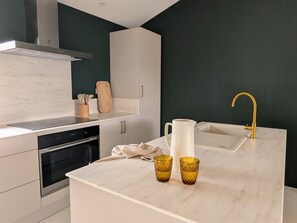 A modern kitchen with a white countertop, a stainless steel oven, a white sink, and a gold faucet.