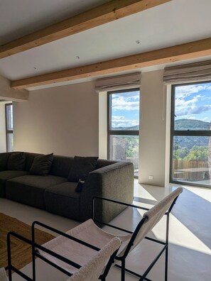 Una sala de estar moderna con un sofá, una silla y grandes ventanales con vistas al exterior.