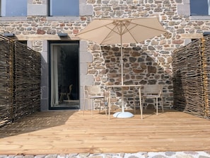 A stone-walled outdoor seating area with a table and chairs, an umbrella, and a wooden deck. - L'Atelier - Maison avec piscine face au volcan (Saint-Just-près-Brioude)