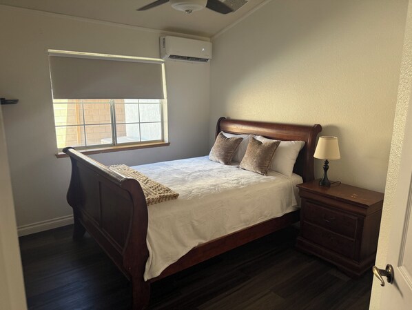 A bedroom with a bed, bedside table, lamp, window, and air conditioning unit.