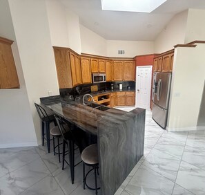 A modern kitchen with a central island, bar stools, wooden cabinets, stainless steel appliances, and a white door.
