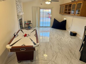 A pool table in a room with a tiled floor, a ceiling fan, and a wooden cabinet.