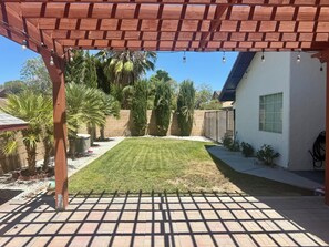 A backyard with a wooden pergola, a lawn, and a brick wall.