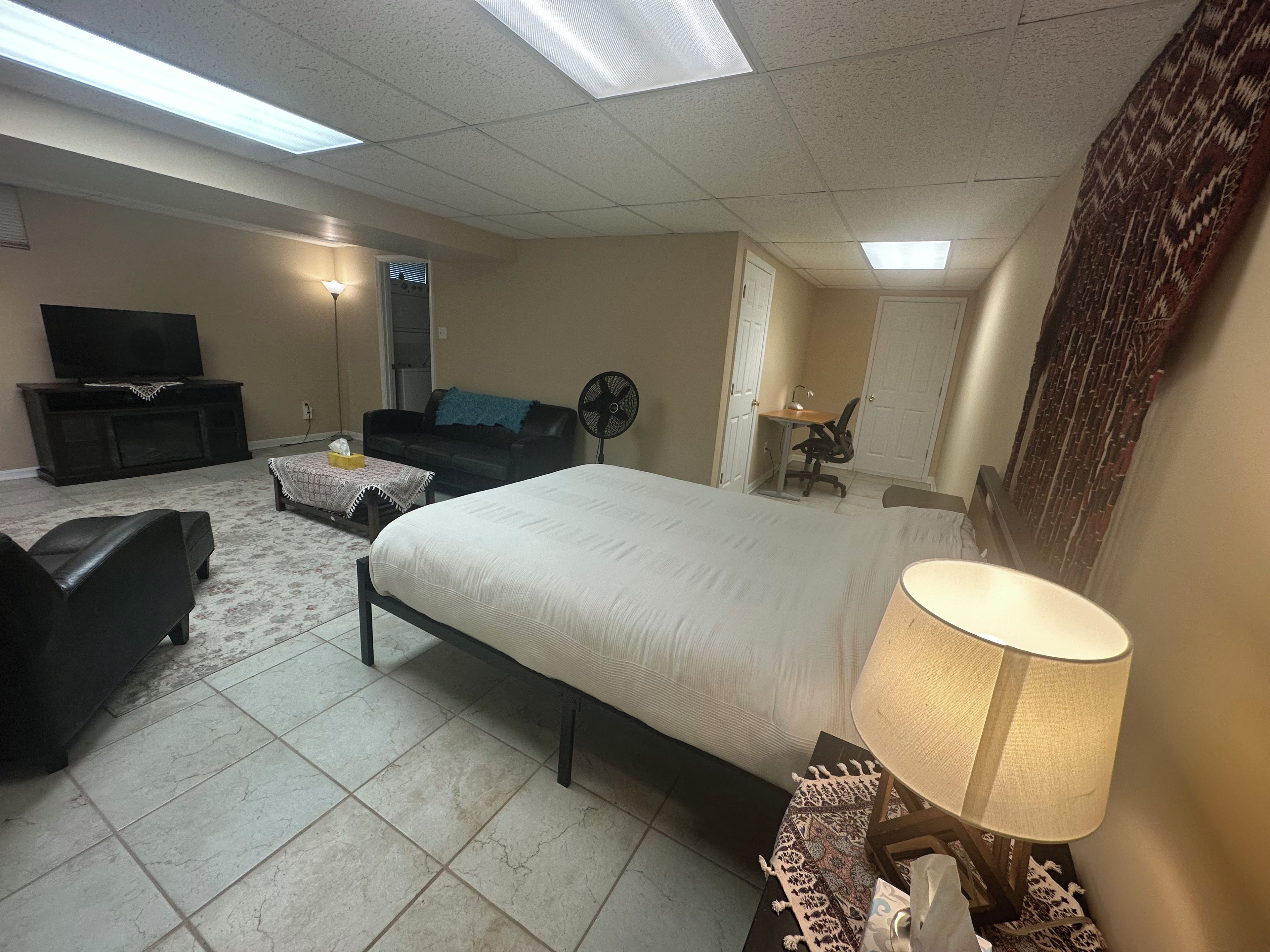 A hotel room with a bed, a desk, a chair, a sofa, a TV, and a fan.