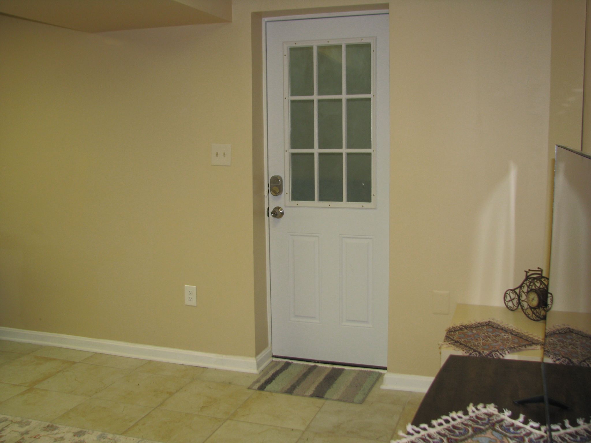 A room with a white door, a patterned rug, and a small table with a decorative item.