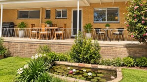 Propiedad residencial con patio cubierto, mobiliario exterior, fachada de ladrillo y un pequeño jardín con estanque.