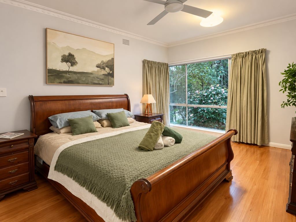 Un dormitorio con una cama de madera, una mesita de noche, una lámpara, una ventana con cortinas y un cuadro en la pared.