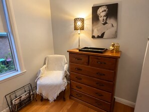 A corner room with a wooden dresser, a lamp, a framed picture, and a window.