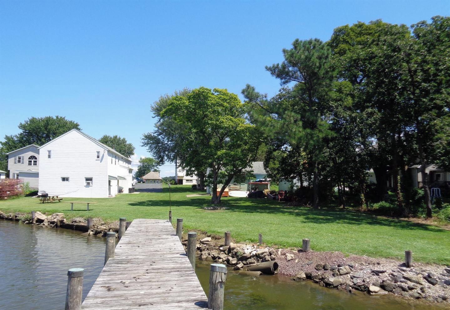 A wooden dock leading to a calm water body, surrounded by grassy areas and trees.