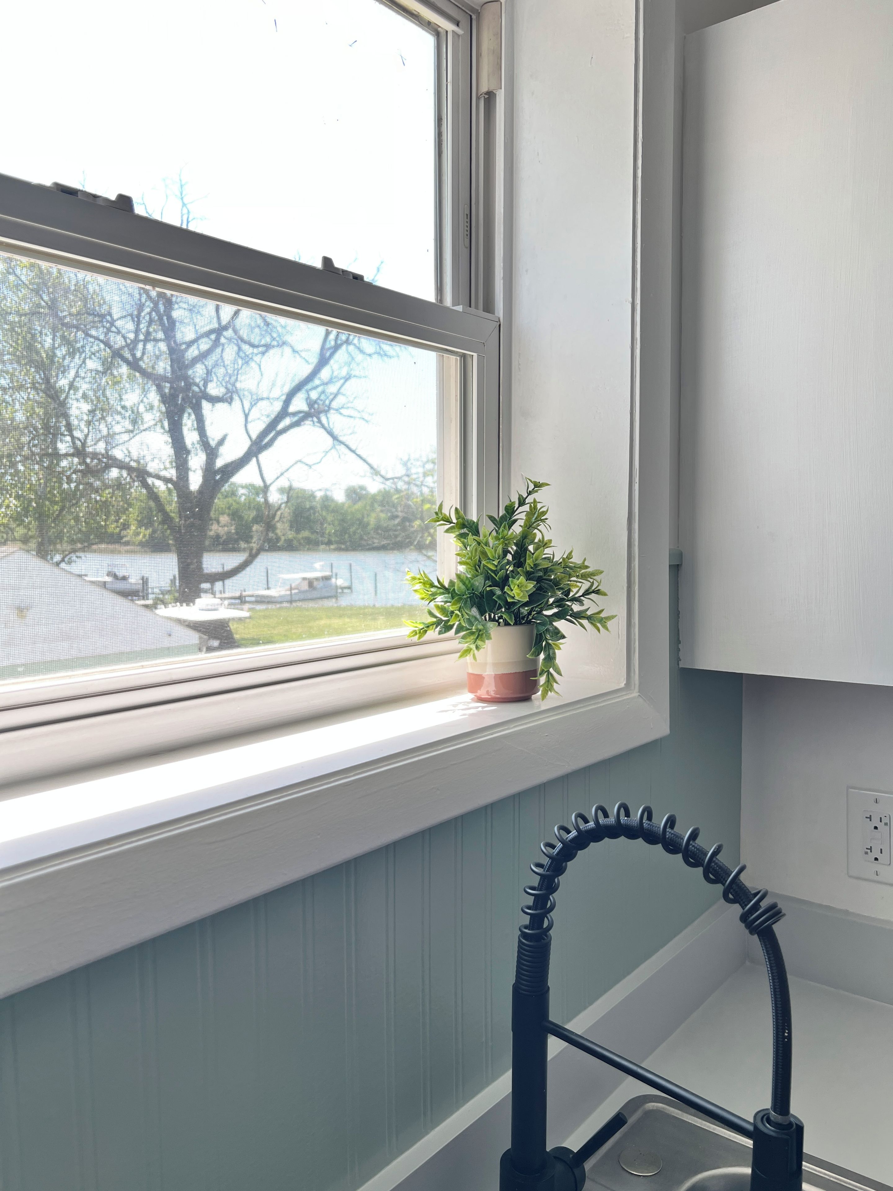 A kitchen with a window, a potted plant, and a faucet.
