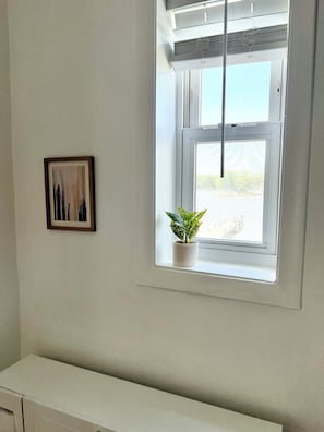 A room with a window, a framed picture on the wall, and a potted plant on the windowsill.