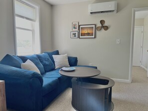 A living room with a blue sofa, a round table, and a wall-mounted air conditioner.