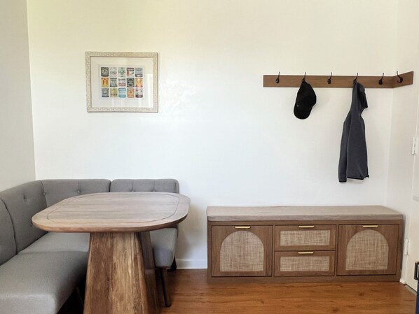 A living room with a grey sofa, a wooden table, a cabinet with drawers, and a coat rack with two coats.