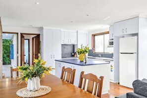 Eine moderne Küche mit weißen Schränken, einem Holztisch mit Stühlen und einer kleinen Kücheninsel mit Blumen.