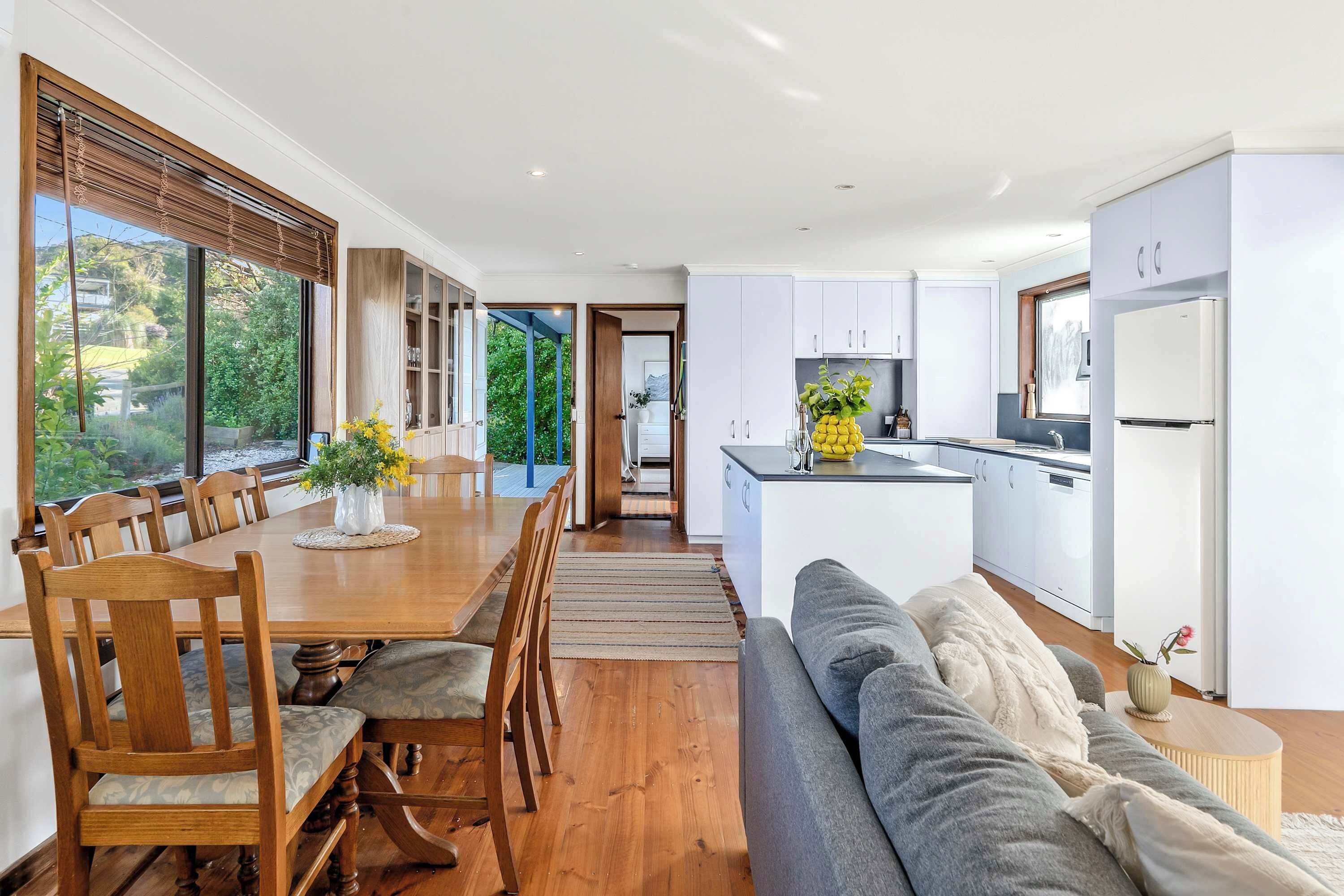 A modern kitchen with white cabinets, a built-in oven, and a dining area with a wooden table and chairs.