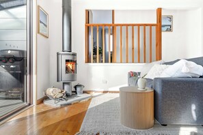 Ein modernes Wohnzimmer mit Kaminofen, einem grauen Sofa und Holzboden.