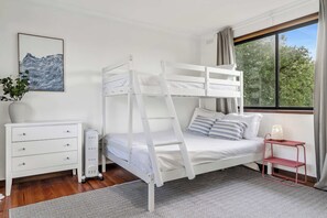 Ein Stockbett mit einer Leiter, ein Nachttisch mit Lampe, eine Kommode und ein Fenster mit Vorhängen.