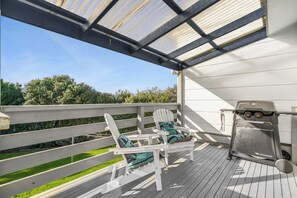 Een overdekt terras buiten met een barbecue en Adirondack-stoelen.