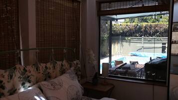 Ein Schlafzimmer mit einem Bett, einem Nachttisch und einem Fenster mit Blick auf einen Garten und Pool.