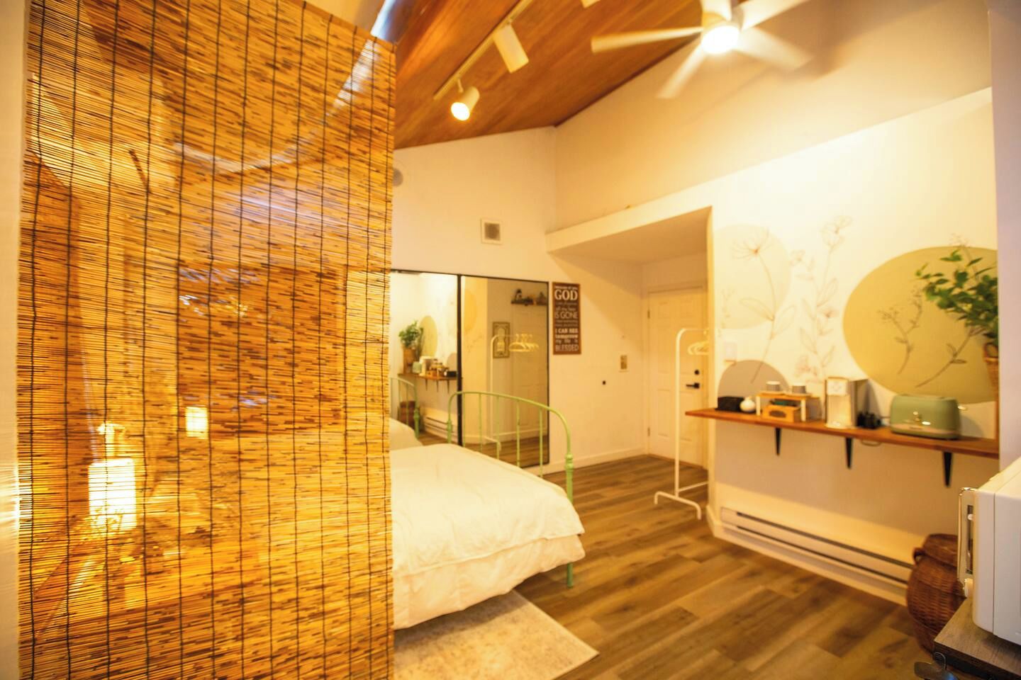 Una habitación de hotel con una cama, un espejo, un estante con objetos y suelo de madera.
