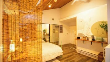 Una habitación de hotel con una cama, un espejo, un estante con objetos y suelo de madera.