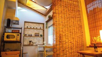 Eine Küche mit Mikrowelle, Regalen voller Küchenutensilien, einem Fenster mit Jalousien und einem Holzstuhl.