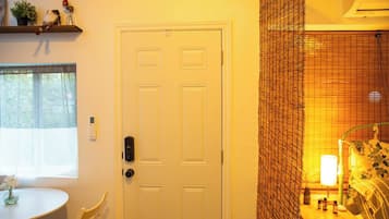 Una habitación con una puerta blanca, una mesita con un florero y una ventana con cortinas translúcidas.
