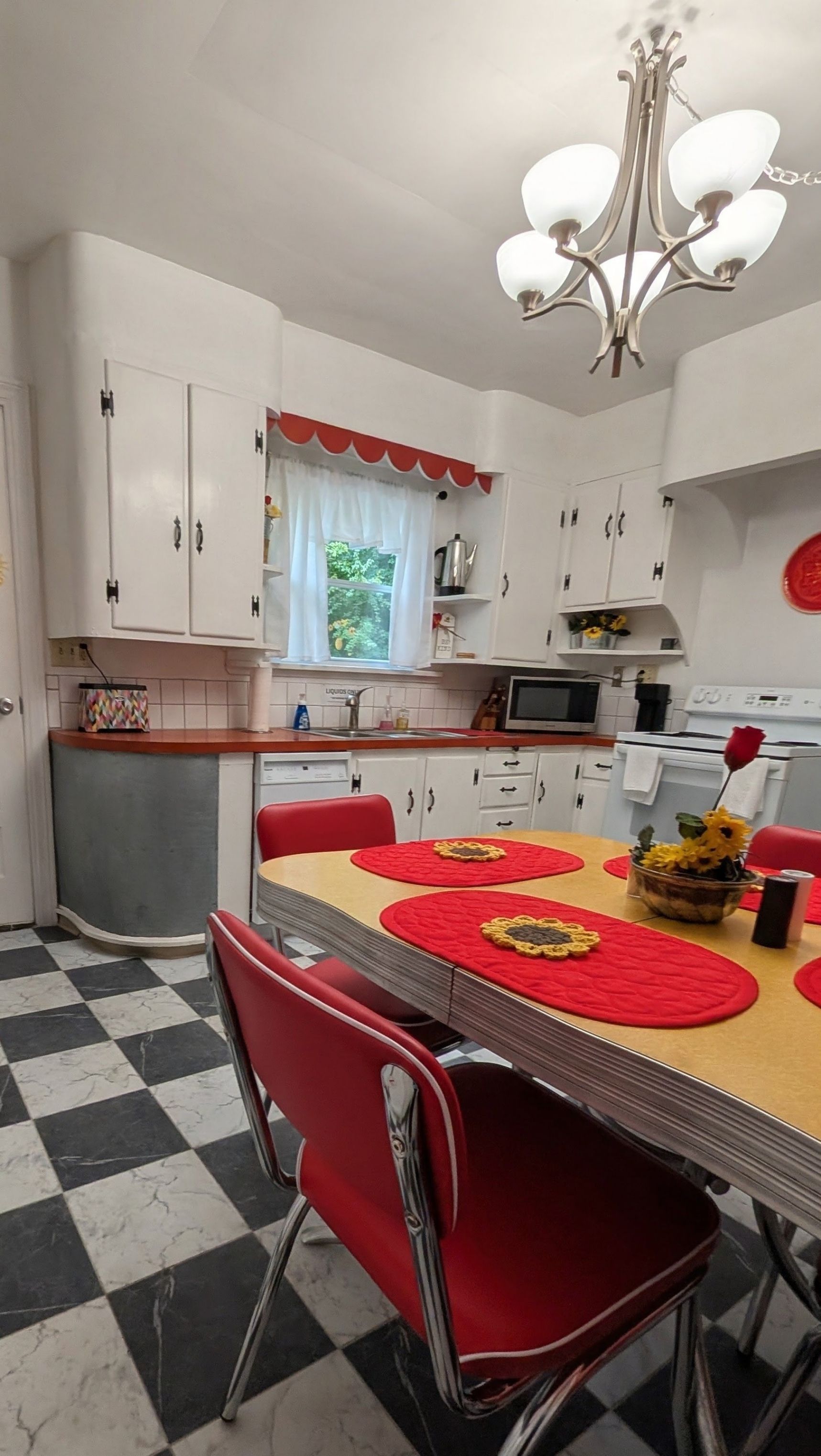 Een keuken met witte kasten, een rode eettafel en een geruit vloertje.