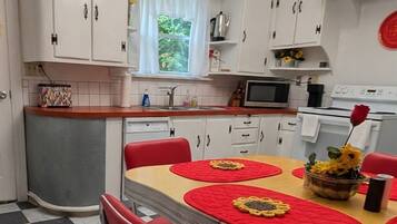 Een keuken met witte kasten, een rode eettafel en een geruit vloertje.