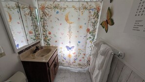 A bathroom with a floral shower curtain, a sink with a mirror, and a towel rack.