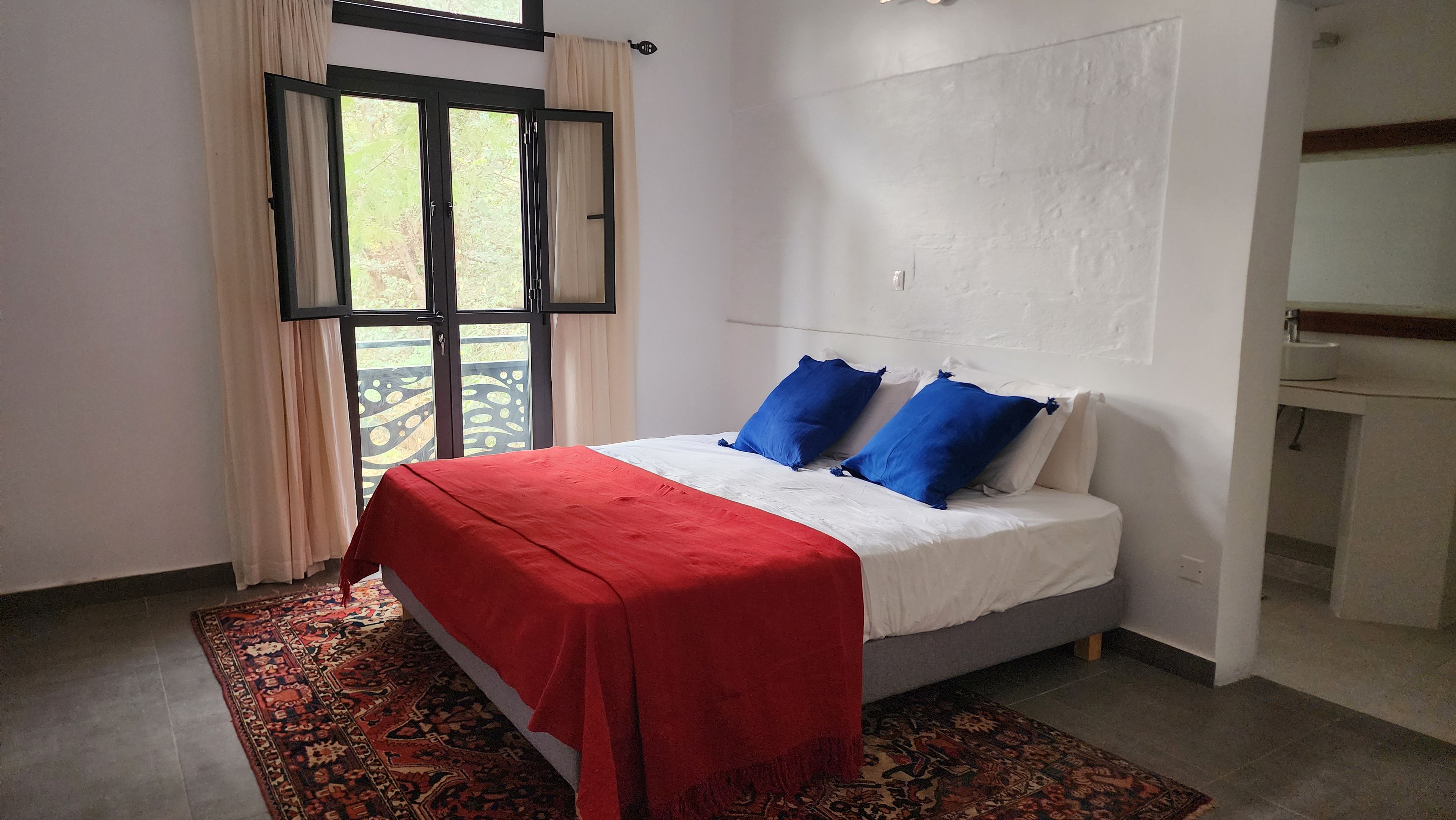 Un dormitorio con una cama, una colcha roja y una alfombra estampada.