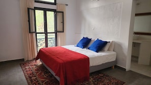 Un dormitorio con una cama, una colcha roja y una alfombra estampada.