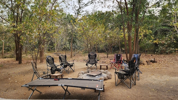 An outdoor camping area with a table and chairs arranged around a central fire pit.