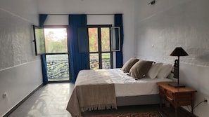 A bedroom with a bed, a nightstand, a lamp, and a view through a window with curtains.