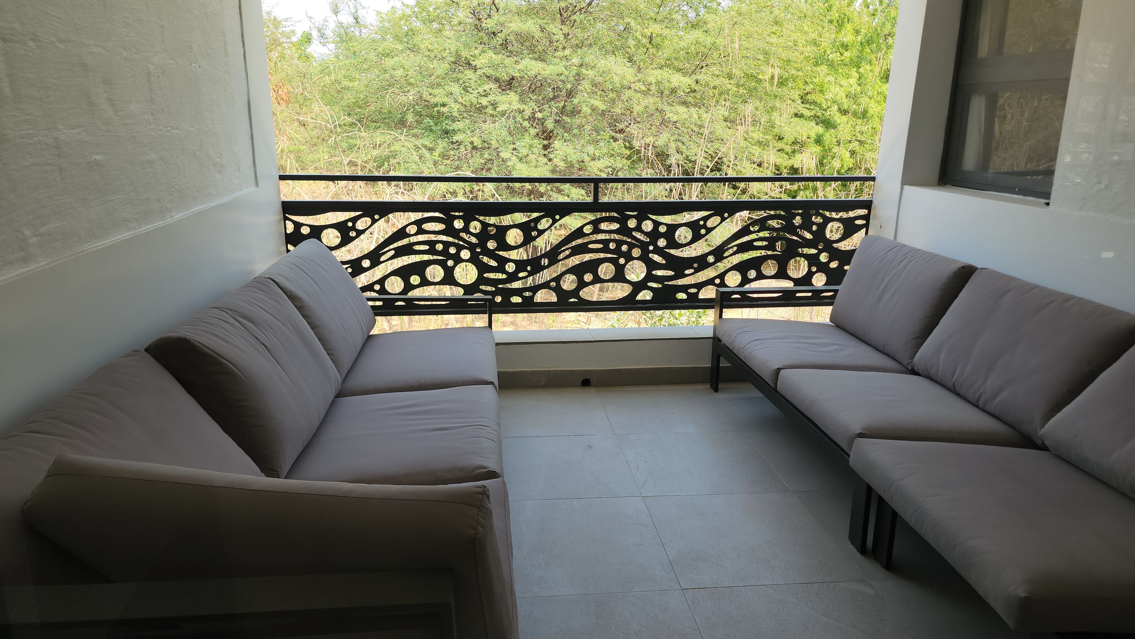 Un balcone con due divani rivolti a una ringhiera decorativa e una vista su alberi.