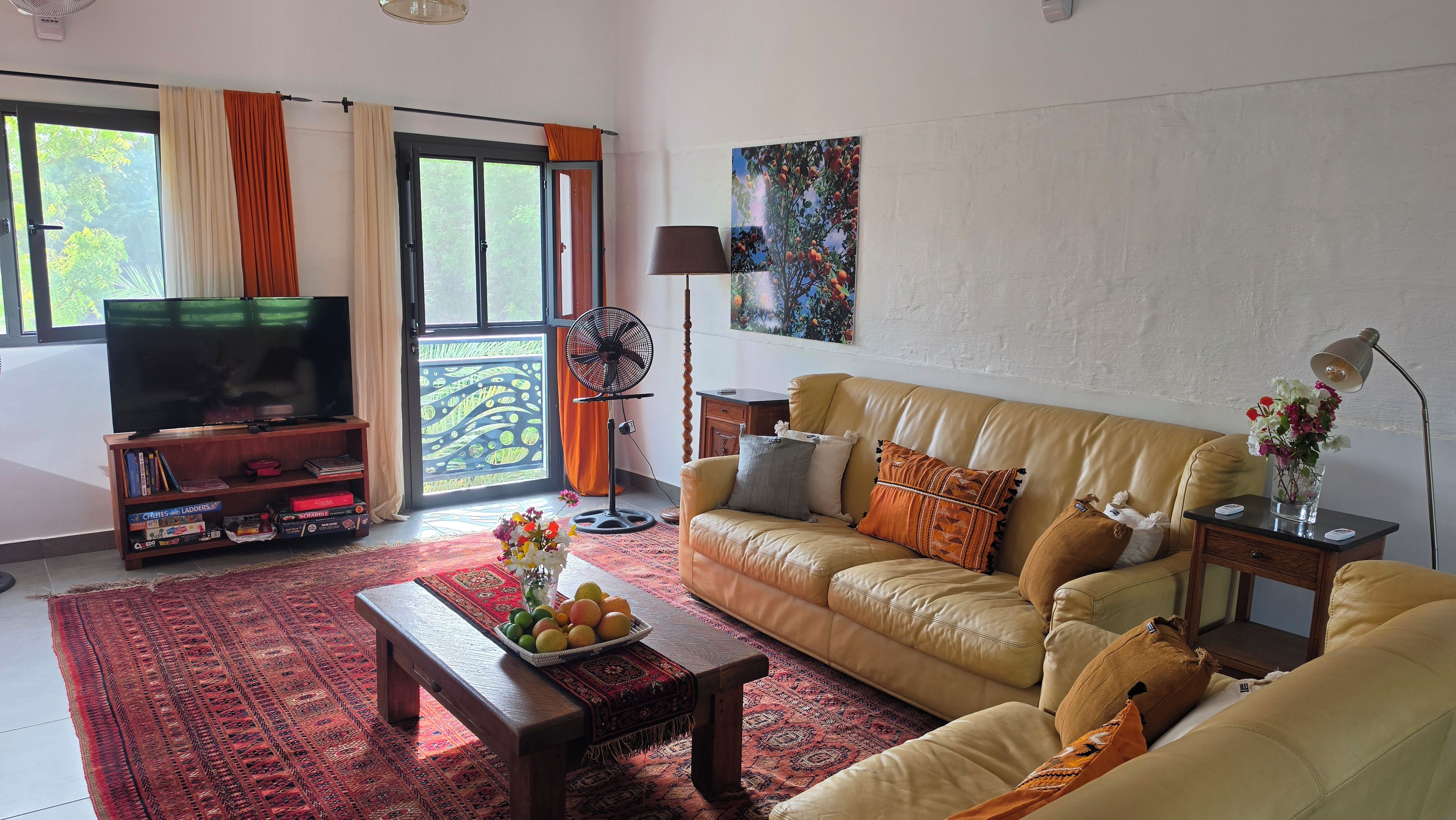 A living room with a sofa, a coffee table with fruit, a TV, and a balcony with curtains.