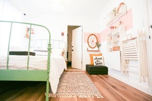 A bedroom with a green metal bed frame, a white bedspread, a patterned rug, a small black ottoman, and a wall with a mirror and a sign that says 'chase the sun'. - Chic Artistic Suite Cozy Luxury w private entry (Richmond)
