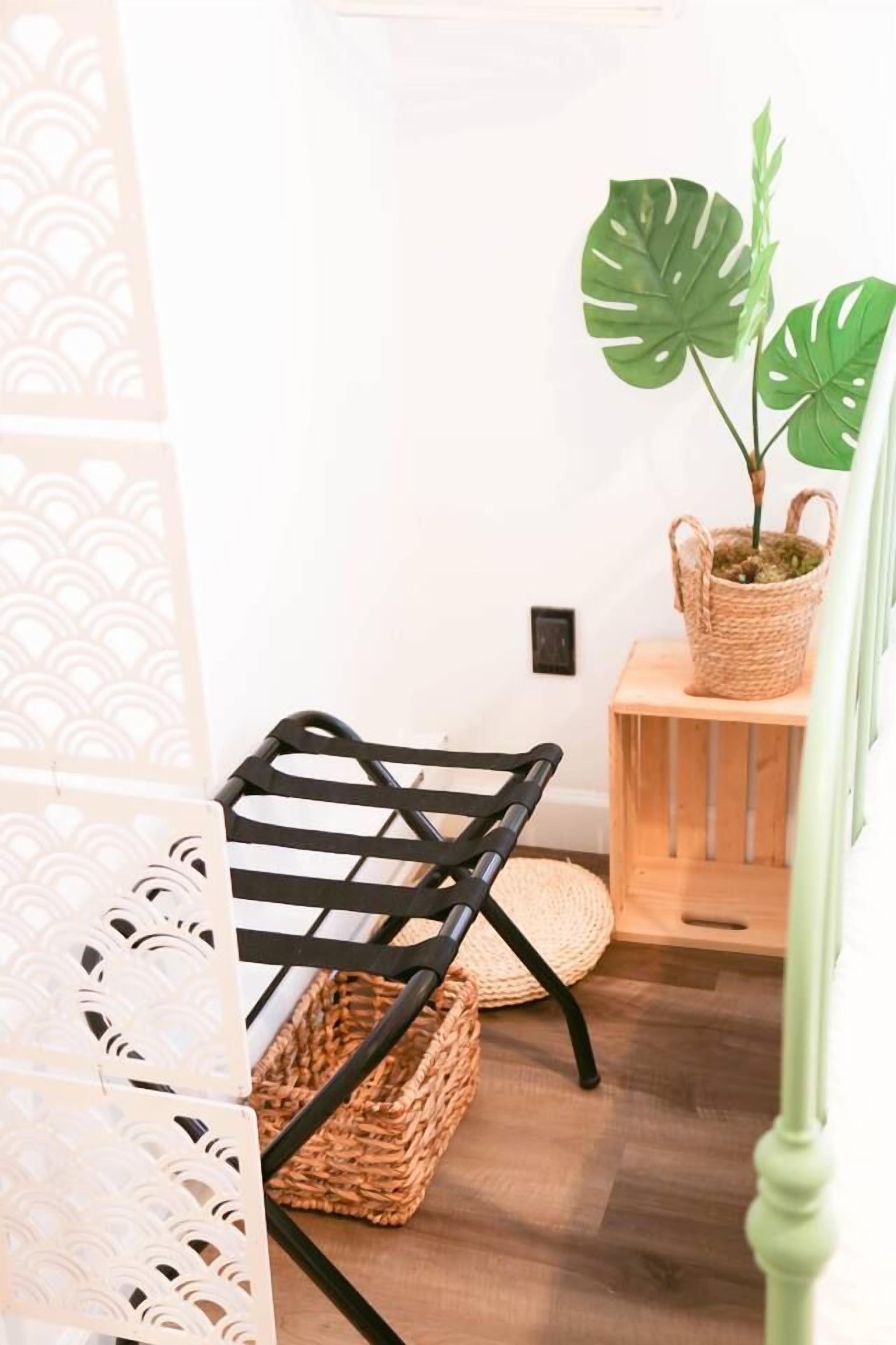 Quarto com uma cadeira de metal preta, uma cesta trançada e uma planta em vaso sobre uma mesa de madeira.