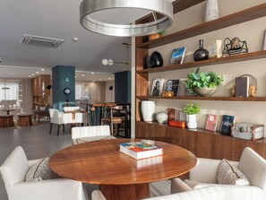 Ein modernes Interieur mit einem runden Holztisch, weißen Stühlen, einem Bücherregal mit verschiedenen Gegenständen und einer Pendelleuchte.