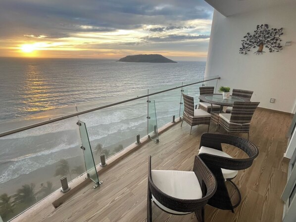 Ein Balkon mit Glastrennwand und Meerblick, ausgestattet mit Korbstühlen und einem Tisch.