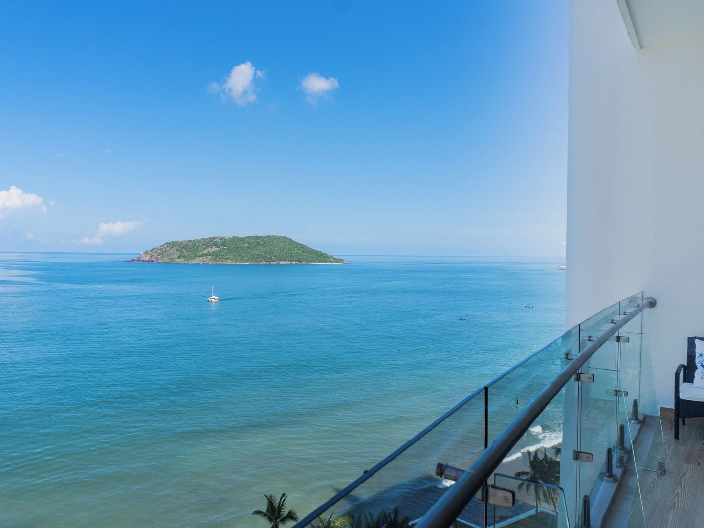 A balcony with a glass railing overlooking a calm sea and a small island.