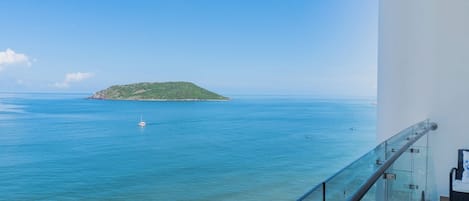 A balcony with a glass railing overlooking a calm sea and a small island.