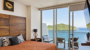 A bedroom with a large bed, a nightstand, a floor lamp, and a view of the sea through a sliding glass door. - Beachfront Luxury | Camino al Mar (Mazatlán)