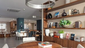 A modern interior with a round wooden table, white chairs, a bookshelf with various items, and a hanging light fixture. - Beachfront Luxury | Camino al Mar (Mazatlán)