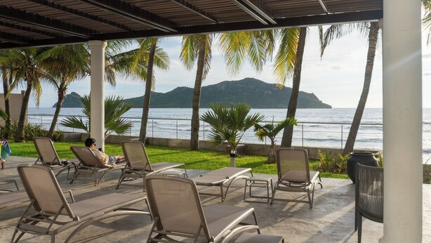 A covered outdoor seating area with lounge chairs and a view of the ocean. - Beachfront Luxury | Camino al Mar (Mazatlán)