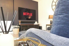 A living room with a grey sofa, a coffee table with remote controls, and a TV displaying the Netflix logo.